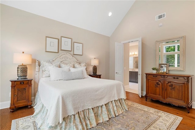 bedroom with dark hardwood / wood-style flooring, high vaulted ceiling, and ensuite bath