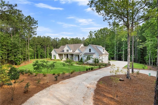 view of front of property featuring driveway, a wooded view, and a front yard