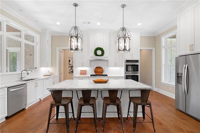 kitchen with a kitchen island, appliances with stainless steel finishes, sink, white cabinets, and light stone countertops