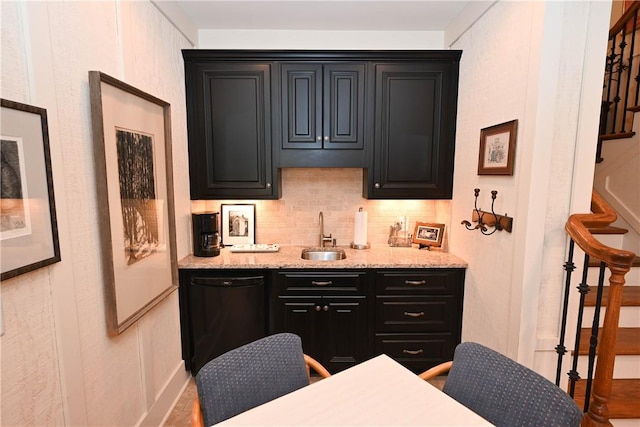 bar featuring backsplash, sink, light stone countertops, and black dishwasher