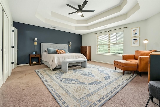 bedroom with a tray ceiling, visible vents, a ceiling fan, baseboards, and light colored carpet