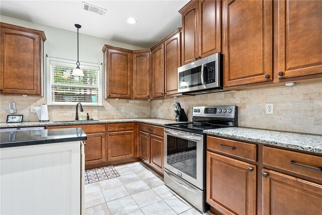 kitchen with light stone counters, a sink, hanging light fixtures, appliances with stainless steel finishes, and visible vents