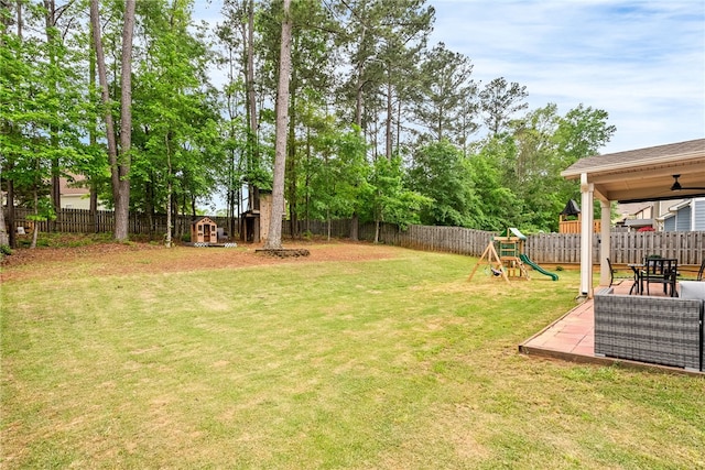 view of yard featuring a playground, a fenced backyard, a storage shed, an outdoor structure, and a patio