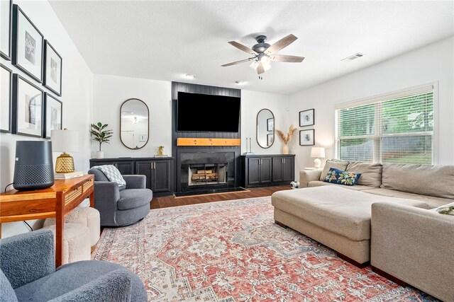 living room with ceiling fan, a large fireplace, wood finished floors, and visible vents