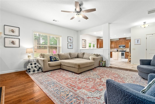 living room featuring light wood-type flooring, visible vents, a ceiling fan, and baseboards