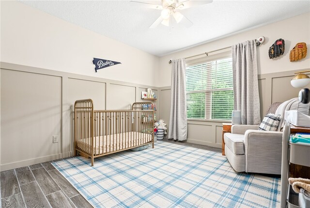 bedroom with wood finished floors, a decorative wall, a crib, and a wainscoted wall