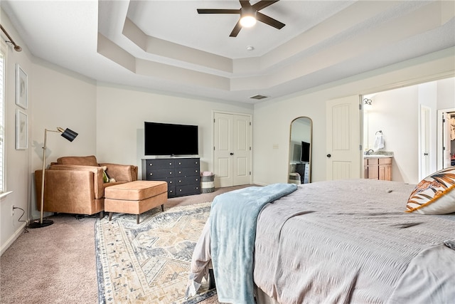 bedroom with a tray ceiling, visible vents, light carpet, arched walkways, and baseboards