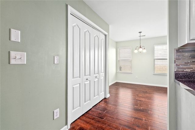 interior space featuring dark wood-type flooring, decorative light fixtures, white cabinets, baseboards, and a chandelier