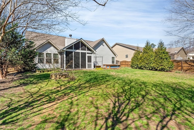 back of house with a lawn, a fenced backyard, a sunroom, a chimney, and a hot tub