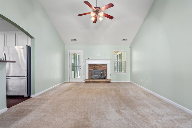 unfurnished living room with visible vents, high vaulted ceiling, a stone fireplace, and carpet