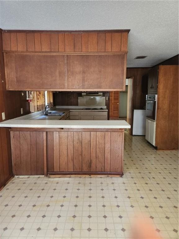 kitchen featuring kitchen peninsula, wooden walls, sink, and oven