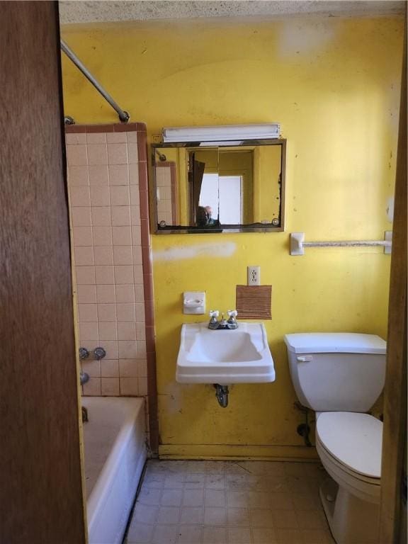 full bathroom featuring a textured ceiling, sink, tiled shower / bath combo, and toilet