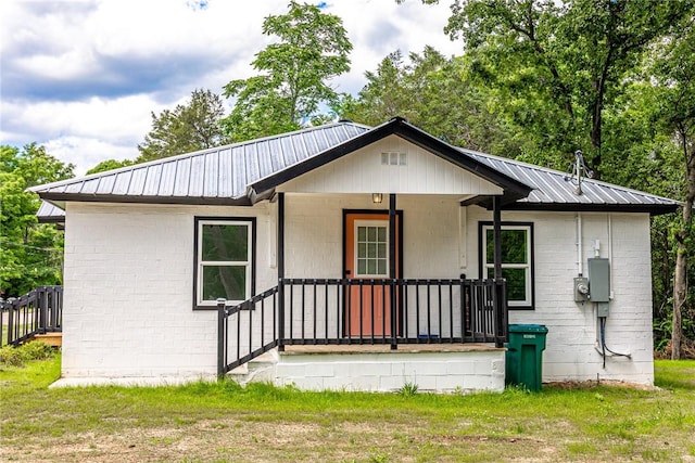 view of front of home with metal roof, a front yard, brick siding, and a porch