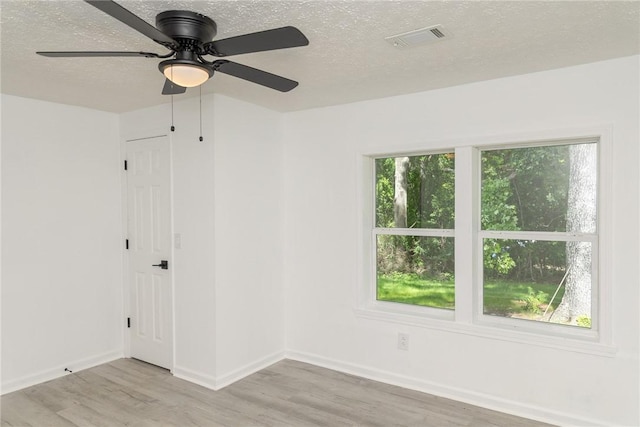 spare room with a textured ceiling, baseboards, visible vents, and light wood-style floors
