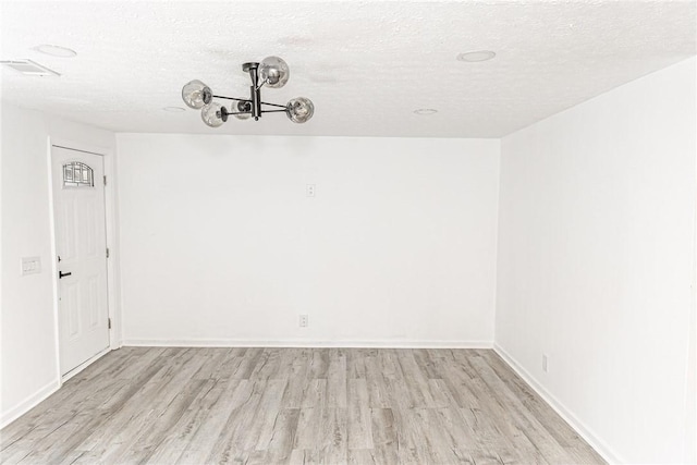 unfurnished dining area with light wood-style floors, a chandelier, baseboards, and a textured ceiling