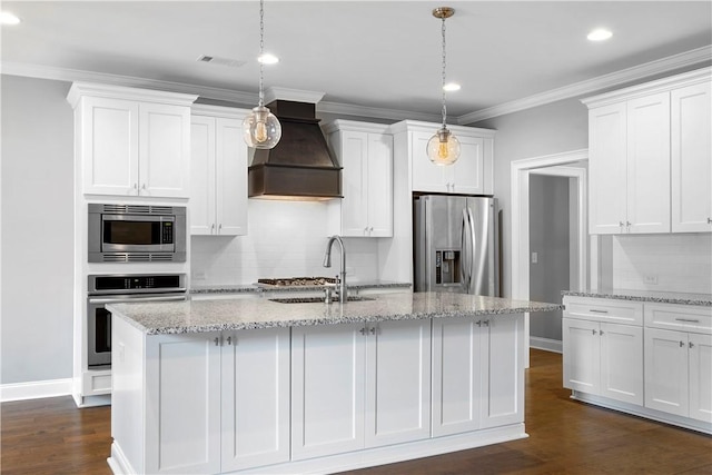 kitchen with custom range hood, an island with sink, appliances with stainless steel finishes, decorative light fixtures, and white cabinetry