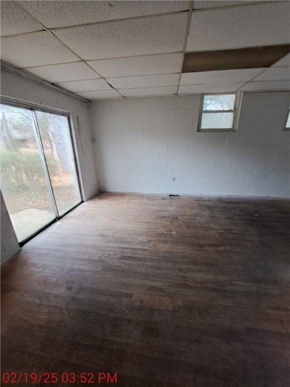 empty room featuring a paneled ceiling, wood finished floors, and concrete block wall