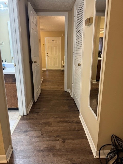 corridor featuring a textured ceiling, dark wood finished floors, and baseboards