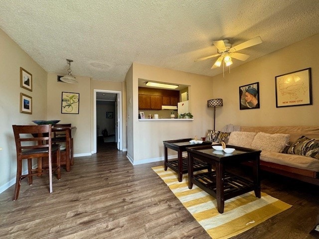 living area with ceiling fan, a textured ceiling, wood finished floors, and baseboards