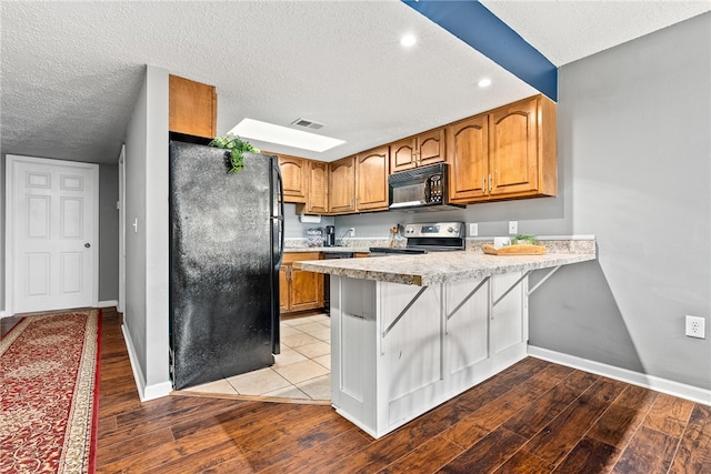 427 Harper Ave Unit 16, Auburn, AL 36830 - kitchen featuring black appliances, a peninsula, light wood-style flooring, light countertops, and a textured ceiling