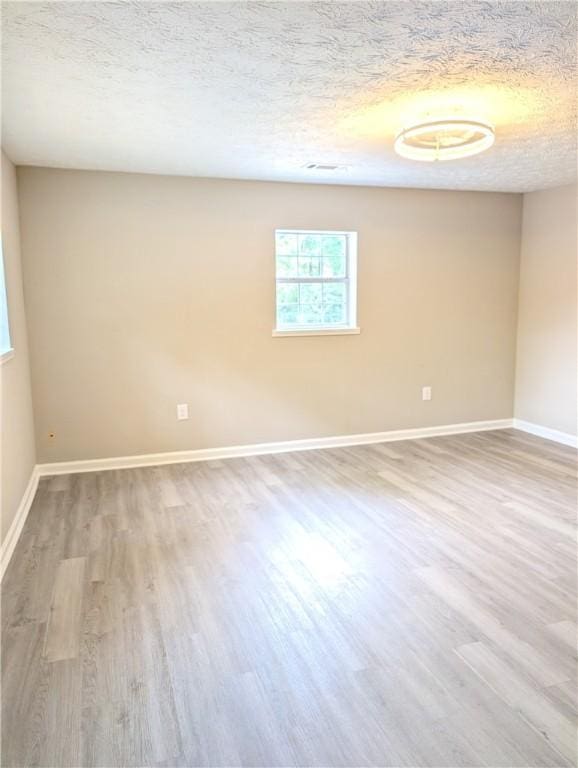 spare room featuring a textured ceiling, wood finished floors, and baseboards