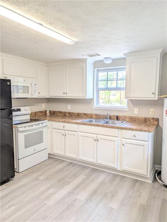 kitchen with a textured ceiling, white appliances, light wood finished floors, a sink, and white cabinets