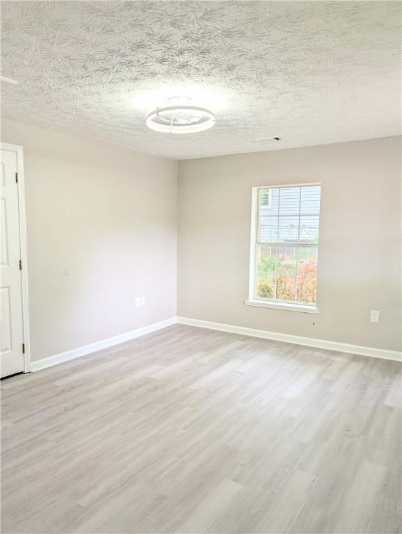 unfurnished room with a textured ceiling, baseboards, and light wood-type flooring