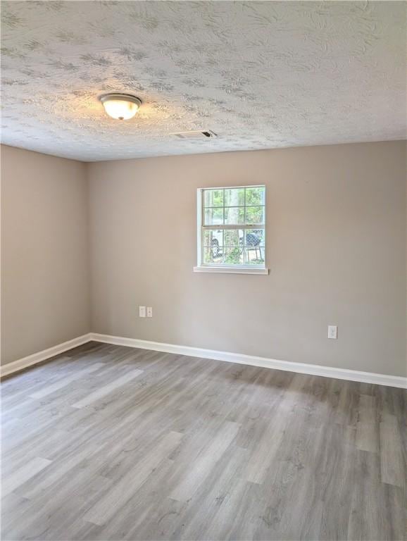 empty room featuring a textured ceiling, wood finished floors, and baseboards