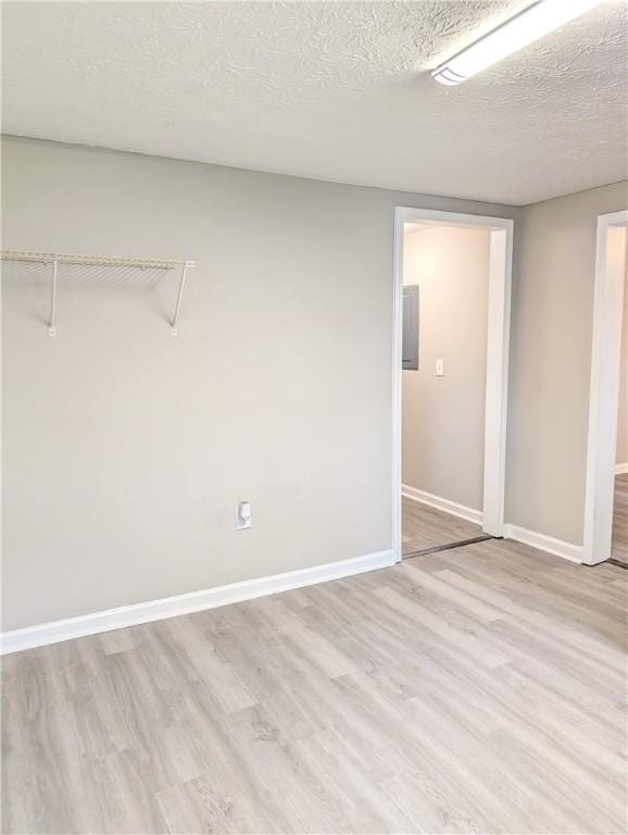 unfurnished room with baseboards, light wood finished floors, and a textured ceiling
