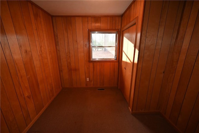 carpeted empty room featuring wood walls