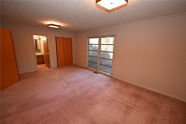 unfurnished bedroom featuring ensuite bathroom, light colored carpet, a textured ceiling, and a closet