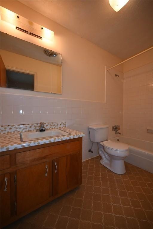 full bathroom with vanity, tiled shower / bath, tile walls, and toilet