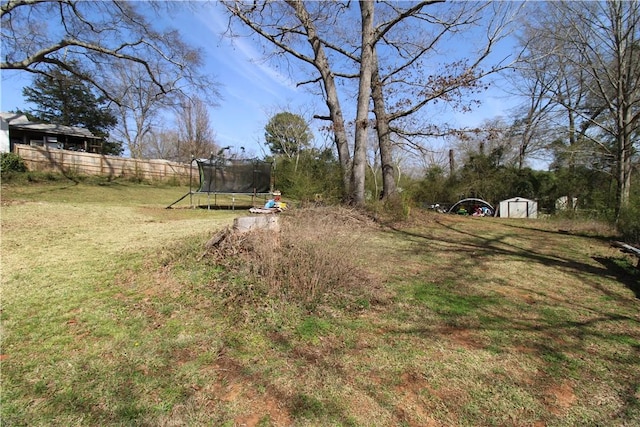 view of yard with an outbuilding, a storage shed, a trampoline, and fence