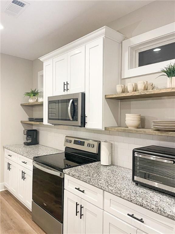 kitchen featuring white cabinetry, light wood-type flooring, light stone counters, and appliances with stainless steel finishes