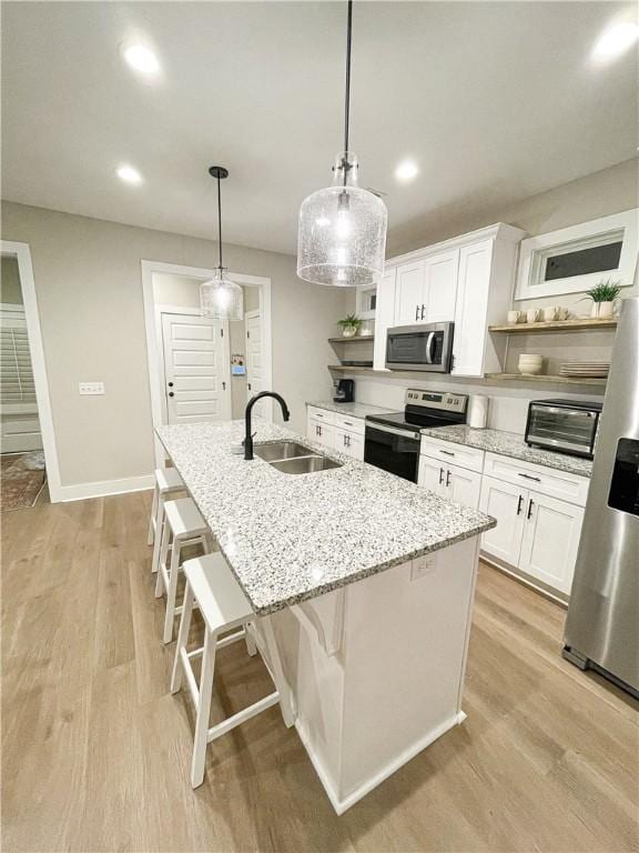 kitchen with appliances with stainless steel finishes, sink, a center island with sink, decorative light fixtures, and white cabinetry