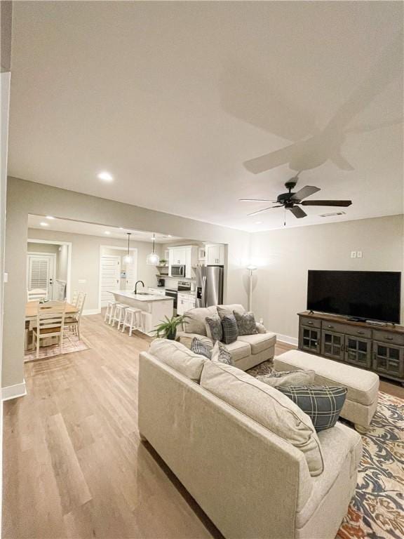 living room with ceiling fan, sink, and light wood-type flooring