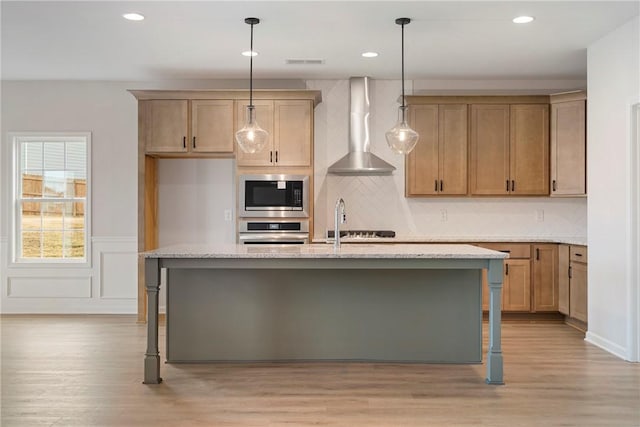 kitchen with wall chimney exhaust hood, hanging light fixtures, a center island with sink, a kitchen breakfast bar, and stainless steel appliances