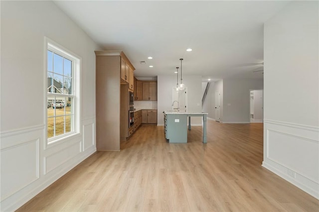 kitchen featuring decorative light fixtures, a kitchen breakfast bar, a kitchen island with sink, and light hardwood / wood-style flooring