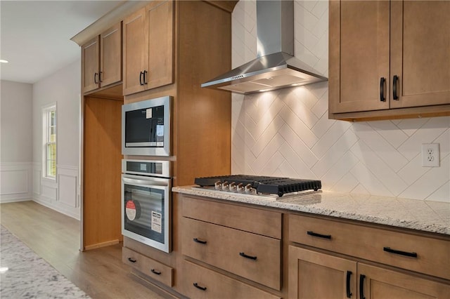 kitchen featuring stainless steel appliances, light stone countertops, wall chimney range hood, and light hardwood / wood-style floors