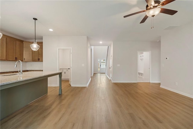 kitchen with pendant lighting, sink, ceiling fan, light stone counters, and light wood-type flooring