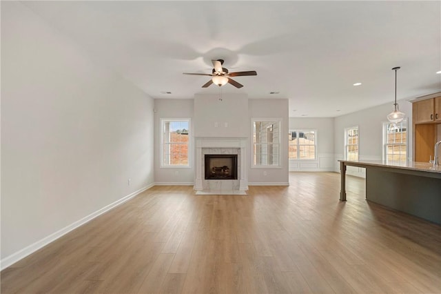 unfurnished living room featuring ceiling fan, sink, a fireplace, and light hardwood / wood-style floors