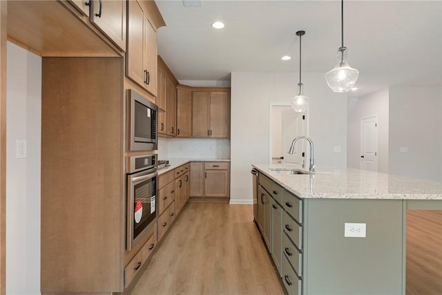 kitchen featuring pendant lighting, sink, appliances with stainless steel finishes, light stone counters, and a center island with sink