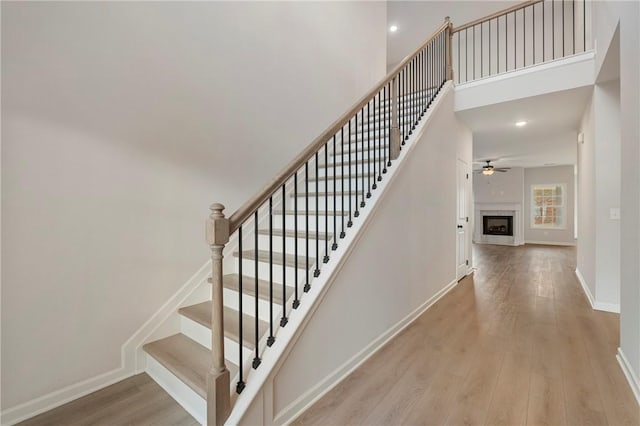 stairs with ceiling fan, a towering ceiling, and wood-type flooring