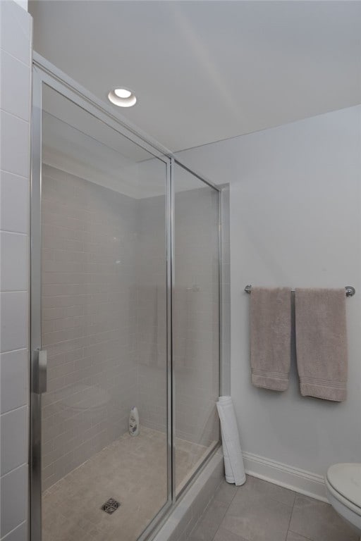 bathroom featuring tile patterned flooring, a shower with door, and toilet