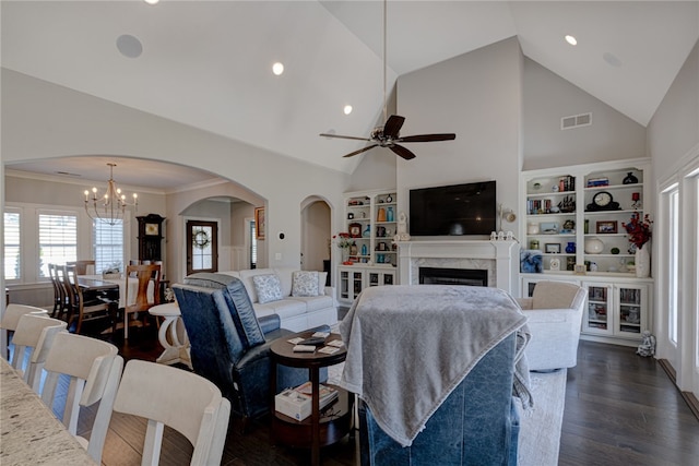 living room with high vaulted ceiling, ceiling fan with notable chandelier, crown molding, built in shelves, and dark hardwood / wood-style floors