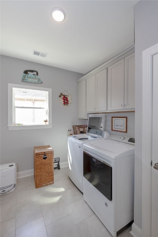 clothes washing area with washing machine and clothes dryer, light tile patterned floors, and cabinets