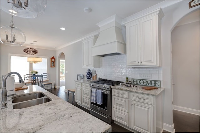 kitchen featuring high end range, custom range hood, sink, pendant lighting, and white cabinets