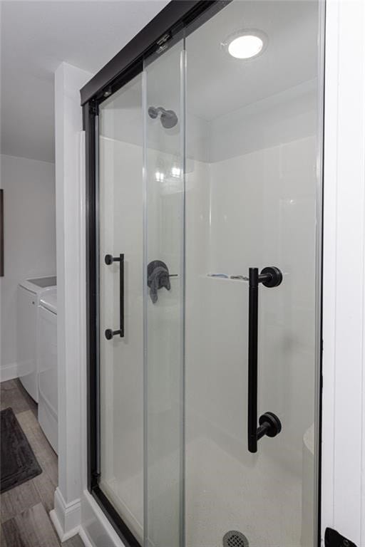 bathroom featuring washing machine and dryer, a shower with shower door, and hardwood / wood-style flooring