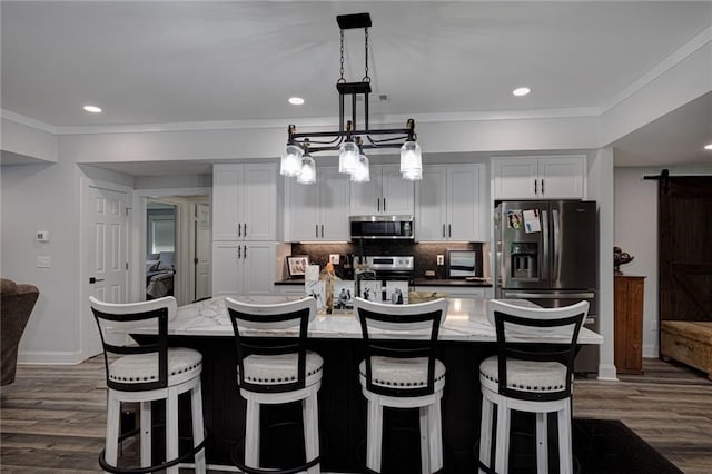 kitchen with a center island with sink, a barn door, stainless steel appliances, and white cabinetry