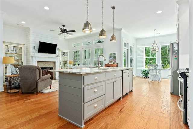 kitchen with a center island with sink, ornamental molding, a sink, stainless steel appliances, and light wood finished floors